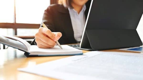 Image of a woman working at a desk using a laptop and making notes in a journal.