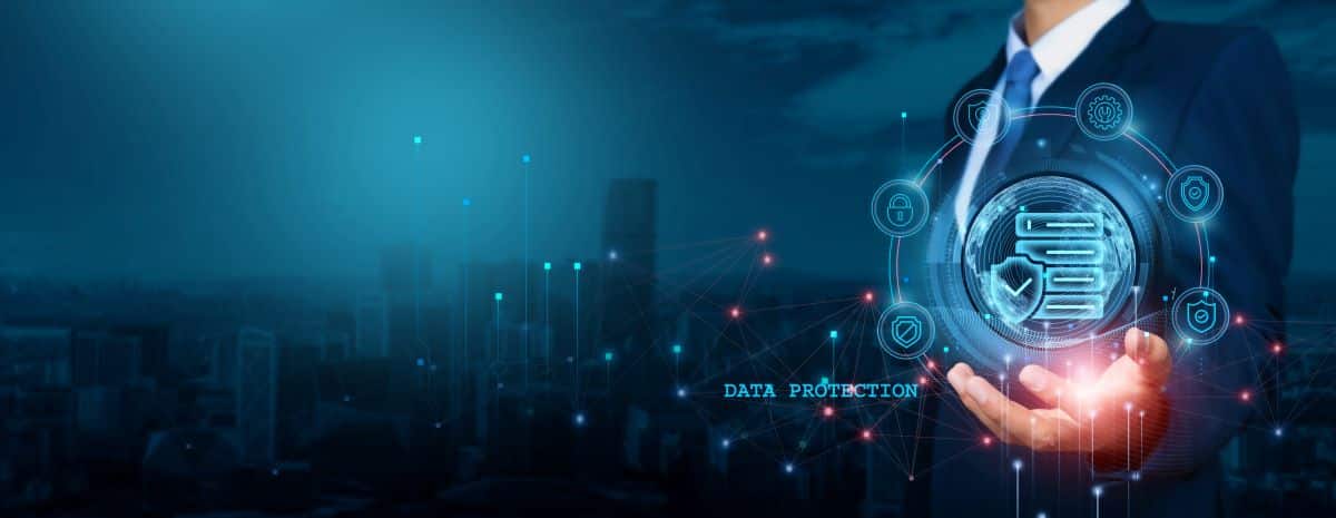 On a background of a hazy blue cityscape, a person in a business suit reaches forward and cups their hand under a graphic with data protection icons.